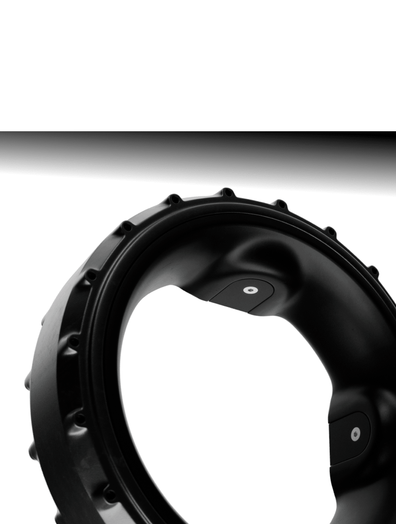 Close-up of a black circular mechanical component with a smooth, glossy surface and evenly spaced raised edges, against a white background. The interior features geometric design elements with circular patterns.