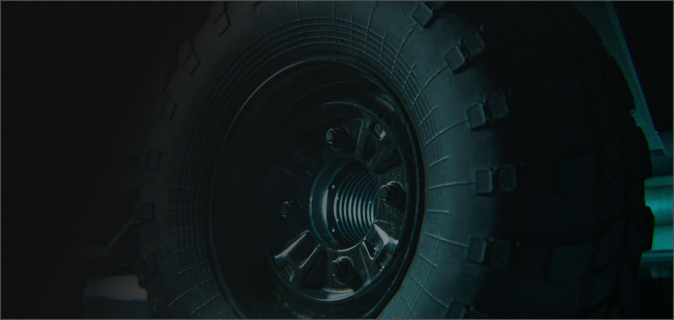 Close-up view of a rugged off-road tire mounted on a vehicle, showing the tread pattern and metal rim in dim lighting.
