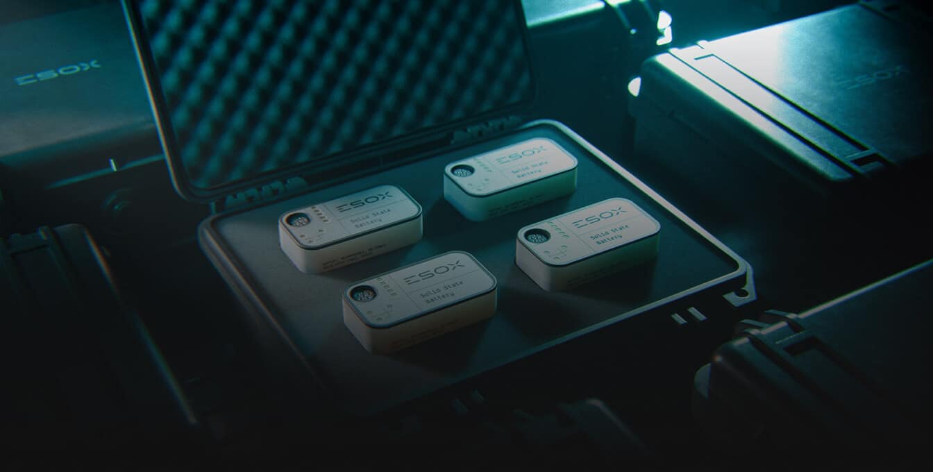 Four small, rectangular devices labeled "ESOX" are neatly arranged inside an open, foam-padded protective case, surrounded by other closed cases in dim, blue-tinted lighting.