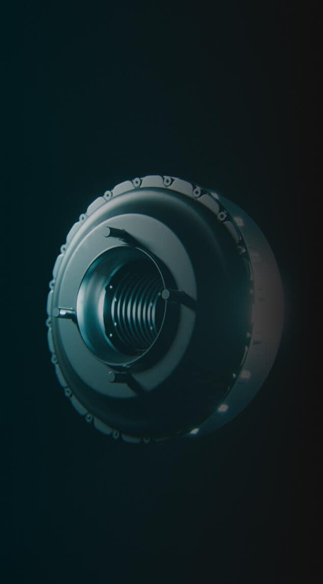 A close-up view of a metallic, circular, turbine-like object with a central spiral structure, illuminated by soft light against a dark background.