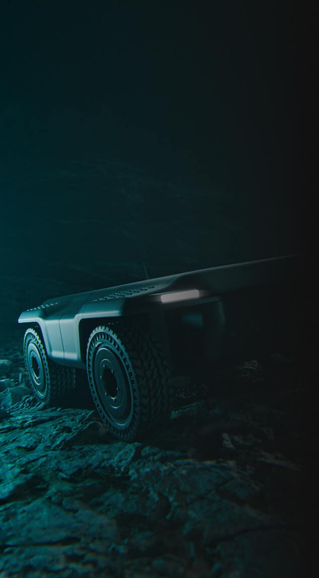 A rugged, futuristic off-road vehicle with large tires is illuminated on rocky terrain in a dimly lit, shadowy environment.