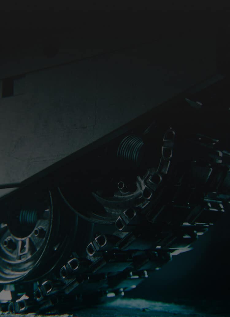 Close-up view of a tank's metal tracks and wheels in low lighting, highlighting the mechanical details and rugged texture of the armored vehicle.