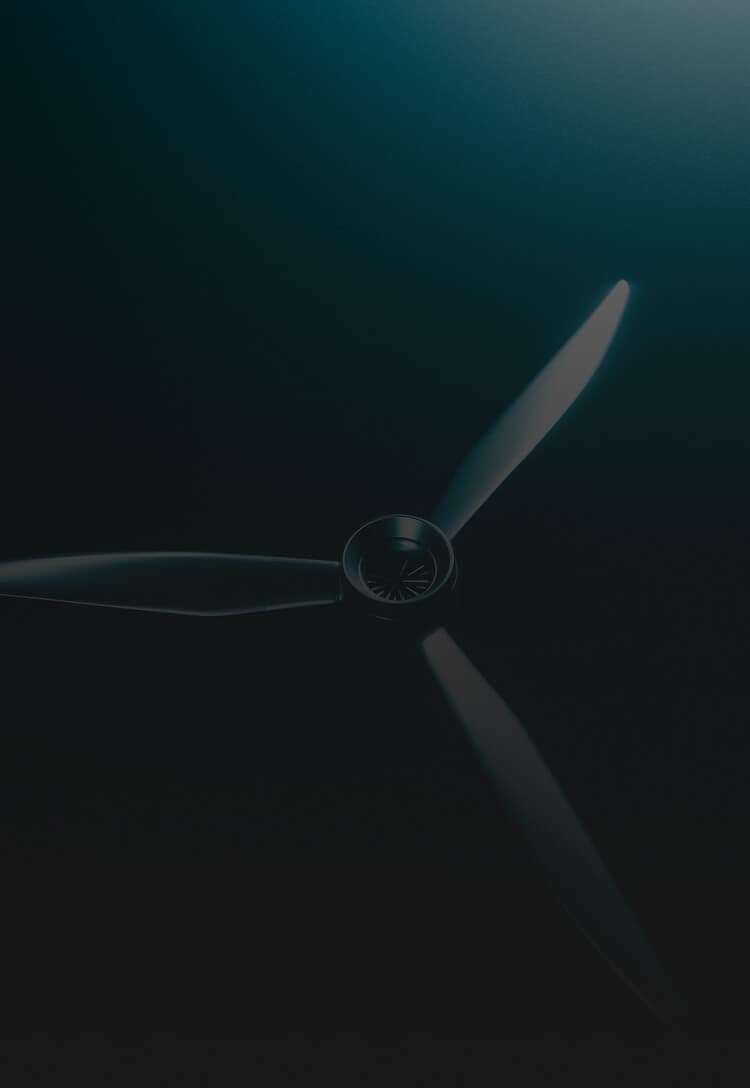 A close-up, top-down view of a three-blade propeller against a dark, gradient background with teal light illuminating the upper part.