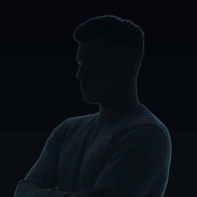 Silhouette of a person with short hair in a dark setting, facing left with arms crossed. The outline is subtly illuminated, highlighting the contours against the black background.