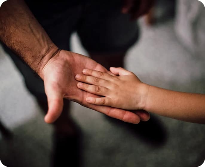A child's hand rests gently on top of an adult's open palm, symbolizing connection and trust. The background is softly blurred, drawing focus to the hands.