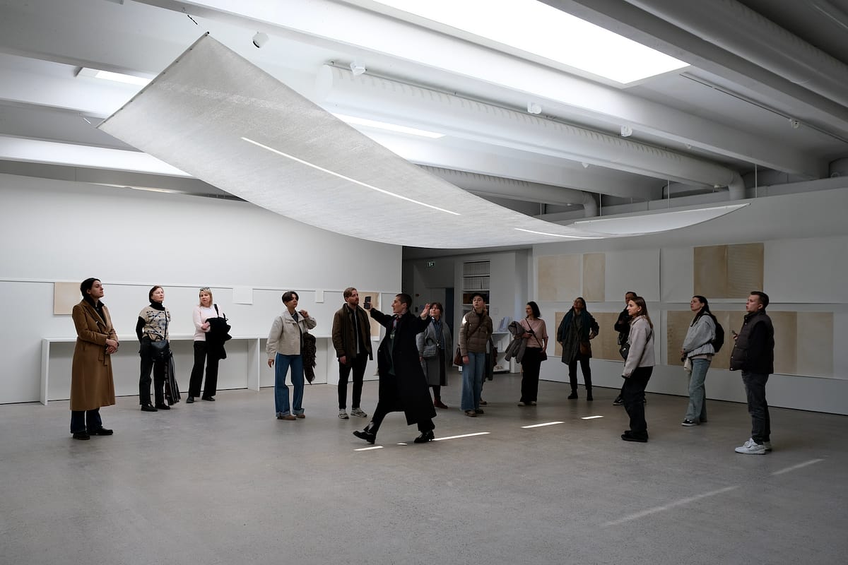 guide with a group of visitors in an exhibition space with a large, white paper work hanging from the ceiling.