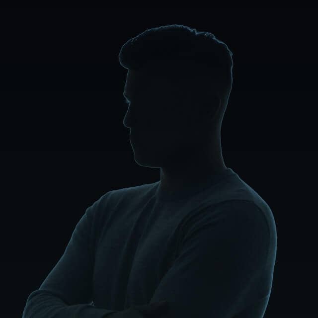 Silhouette of a person with short hair in a dark setting, facing left with arms crossed. The outline is subtly illuminated, highlighting the contours against the black background.