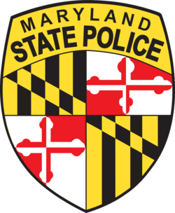 Maryland State Police badge featuring the Maryland flag’s black, gold, red, and white patterns, with “Maryland State Police” written in bold black letters on a yellow background at the top.