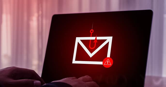 A person types on a laptop displaying an envelope icon with a red phishing hook and warning symbol, indicating a potential email security threat or phishing attack.