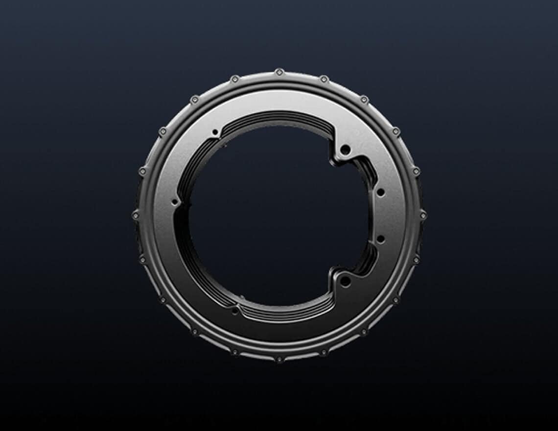 A metallic, circular mechanical component with bolts around its edge and an open section, displayed against a dark gradient background.