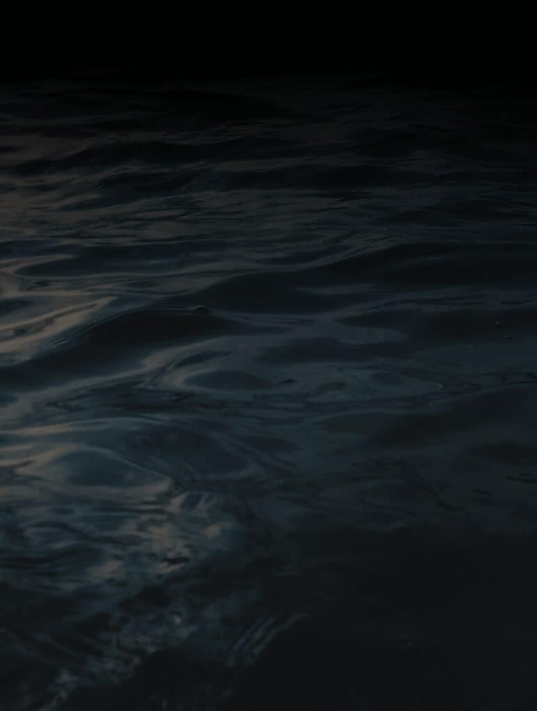 Dark, rippling water with subtle reflections under low light, creating a serene yet mysterious atmosphere.