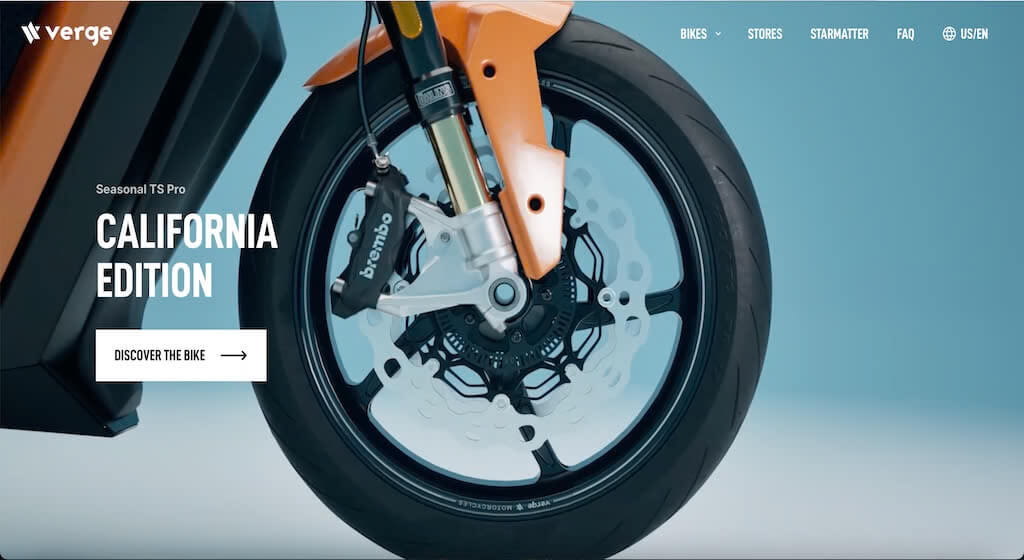 Verge Close-up of the front wheel and orange fender of a Verge electric motorcycle, with “California Edition” and a button reading “Discover the Bike” on the left side. Blue background.