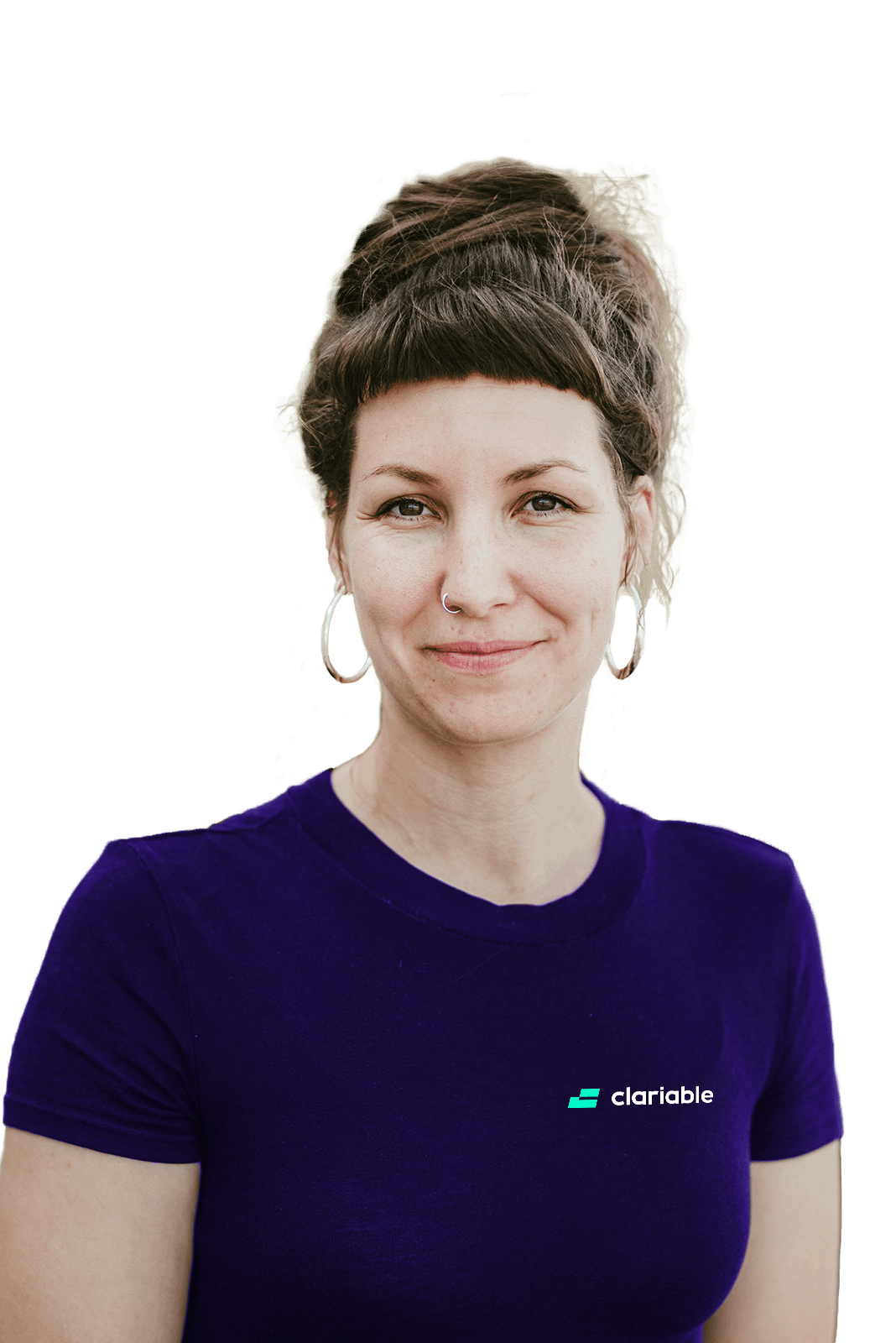 Valena A woman with brown hair in a bun, wearing hoop earrings and a purple "clarable" t-shirt, stands outdoors and smiles softly at the camera with green foliage blurred in the background.