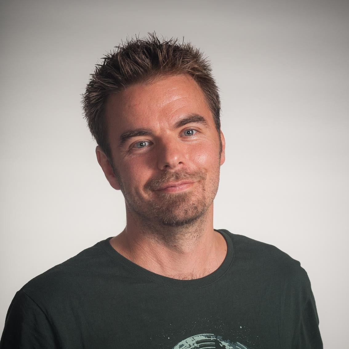 Janne Jussila A man with short brown hair and light stubble smiles slightly, wearing a dark T-shirt. The background is plain and light-colored.