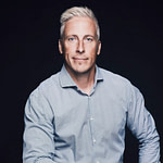 Pekka Kari A man with short, light blond hair and light eyes wears a light blue button-up shirt and poses against a plain dark background, looking confidently at the camera.