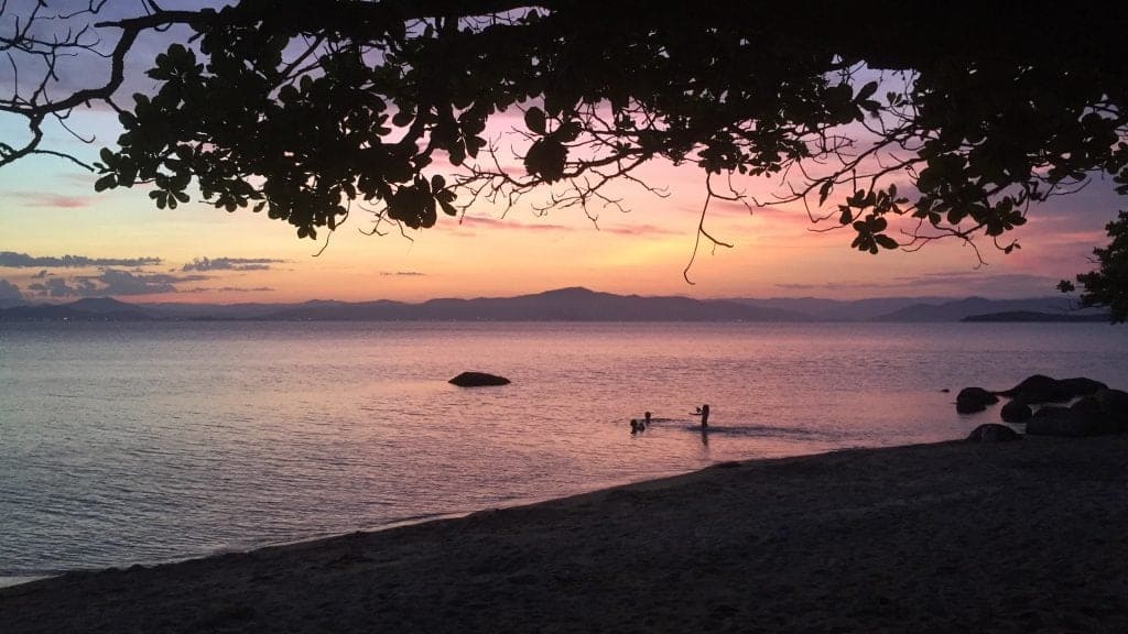 A sunset on a beach with a person on a canoe.