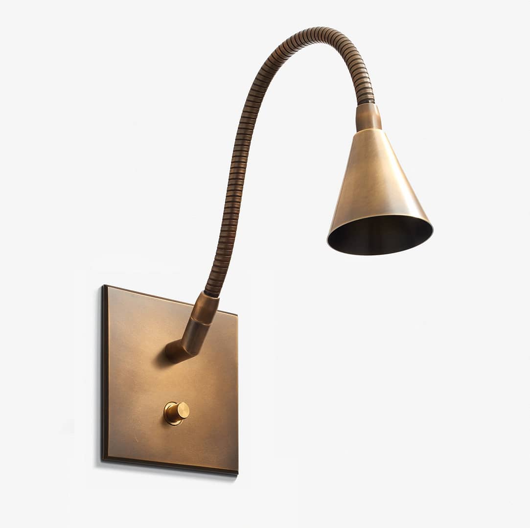A modern, bronze-colored wall-mounted lamp with a flexible neck and a conical shade, illuminated, against a plain white background.
