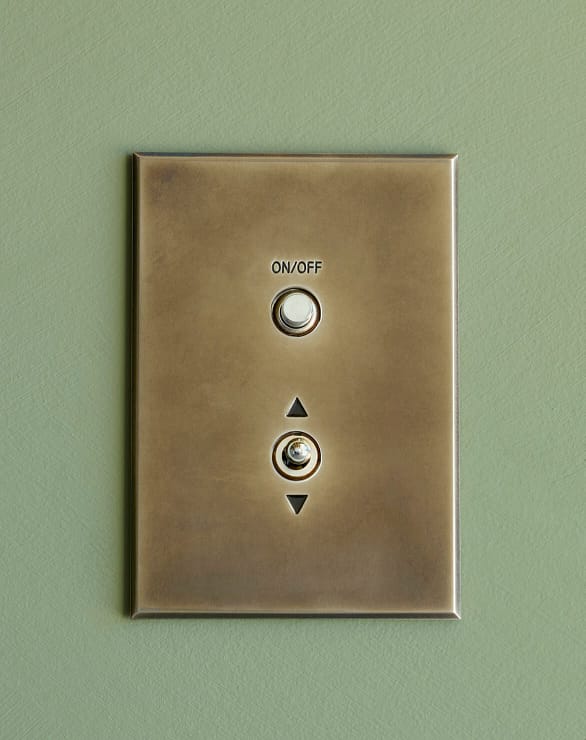 A brass light switch plate with two round buttons labeled "ON/OFF" and an arrow pointing up and down, mounted on a green wall.