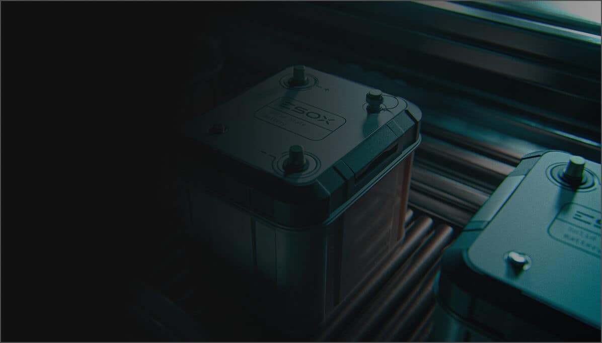 Close-up of two rectangular batteries with metallic tops, labeled “SOX,” placed on a metal surface under low, moody lighting. The left side of the image is mostly dark, with the batteries illuminated from above.