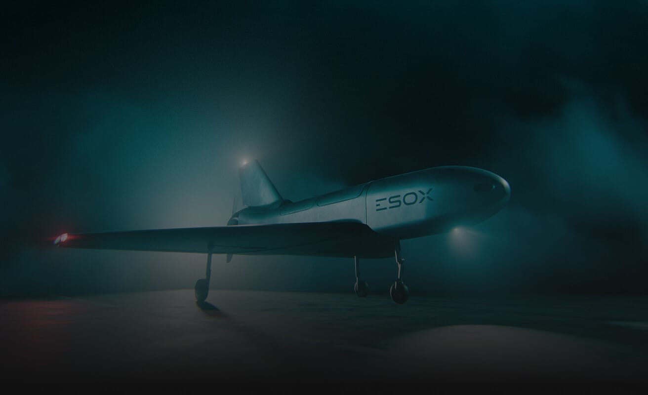 A sleek, futuristic unmanned aircraft labeled "ESOX" stands on a dimly lit runway, illuminated by moody blue and green lighting, with mist or fog in the background.