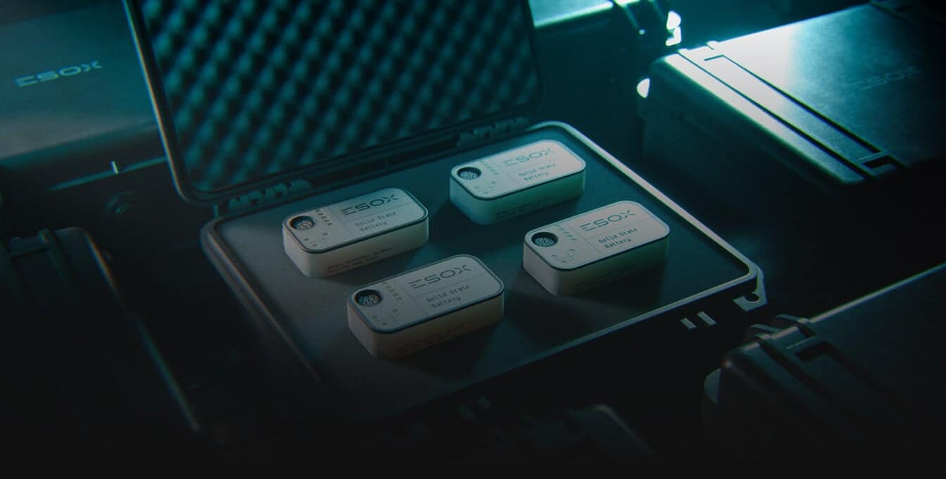 Four small, rectangular devices labeled "ESOX" are neatly arranged inside an open, foam-padded protective case, surrounded by other closed cases in dim, blue-tinted lighting.