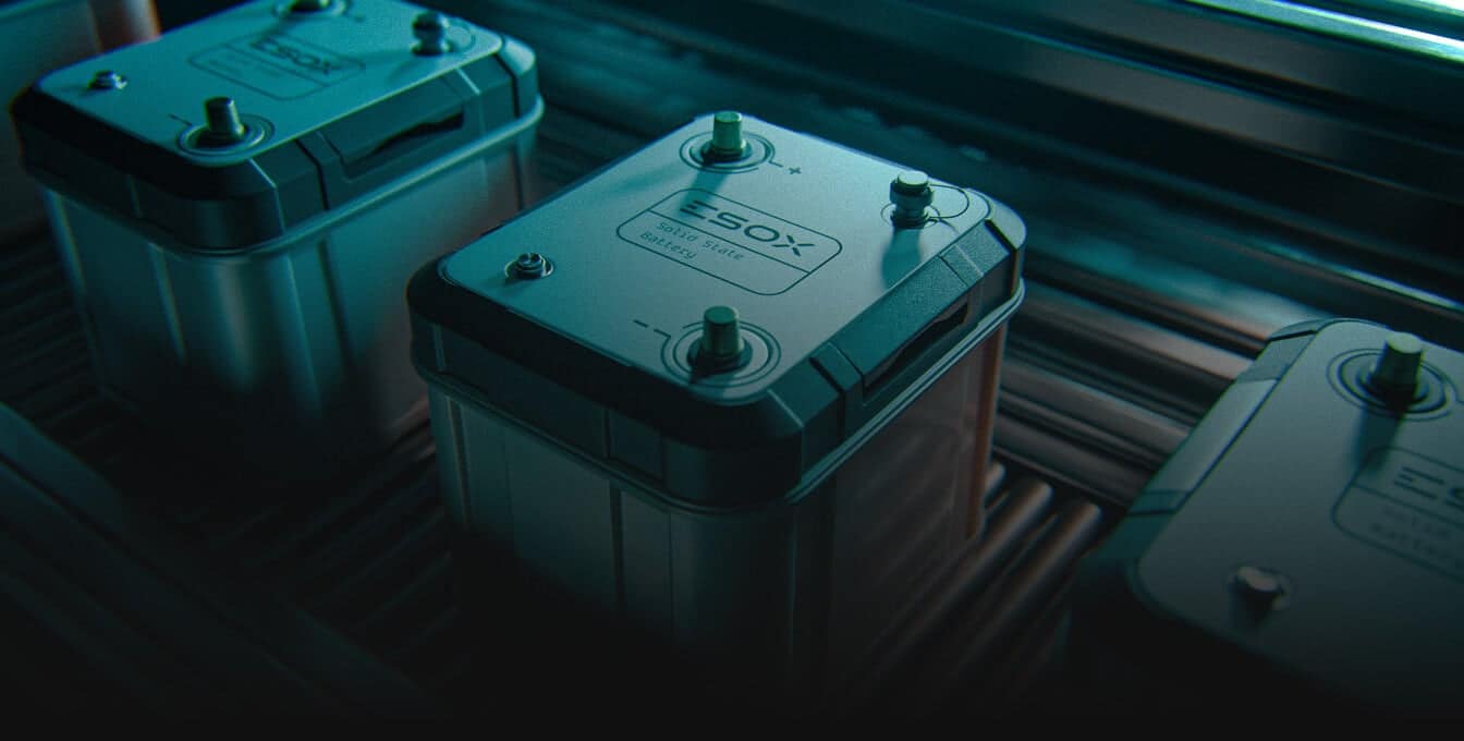 Close-up of several rectangular batteries with metal terminals on top, labeled “SOX,” placed in a row on a conveyor or metal surface under industrial lighting.