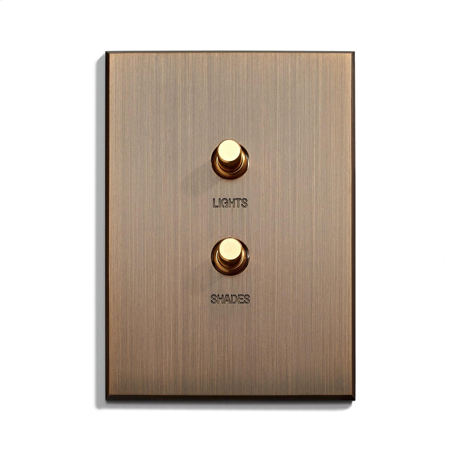 A brass-colored light switch plate with two round toggle switches. The upper switch is labeled "LIGHTS" and the lower switch is labeled "SHADES." The plate has a brushed metal texture.