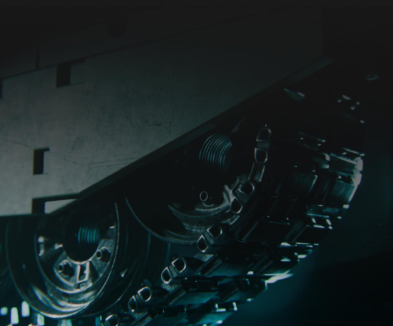 Close-up view of a tank’s metal tracks and wheels in dim lighting, showing mechanical details and a rugged, industrial texture.