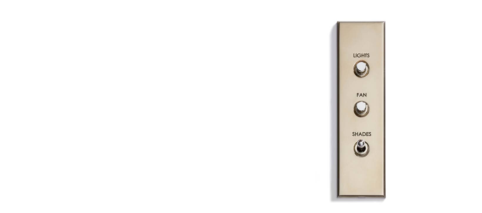 A beige wall switch panel with three labeled toggle switches: "LIGHTS" at the top, "FAN" in the middle, and "SHADES" at the bottom, mounted on a white wall with ample empty space on the left.