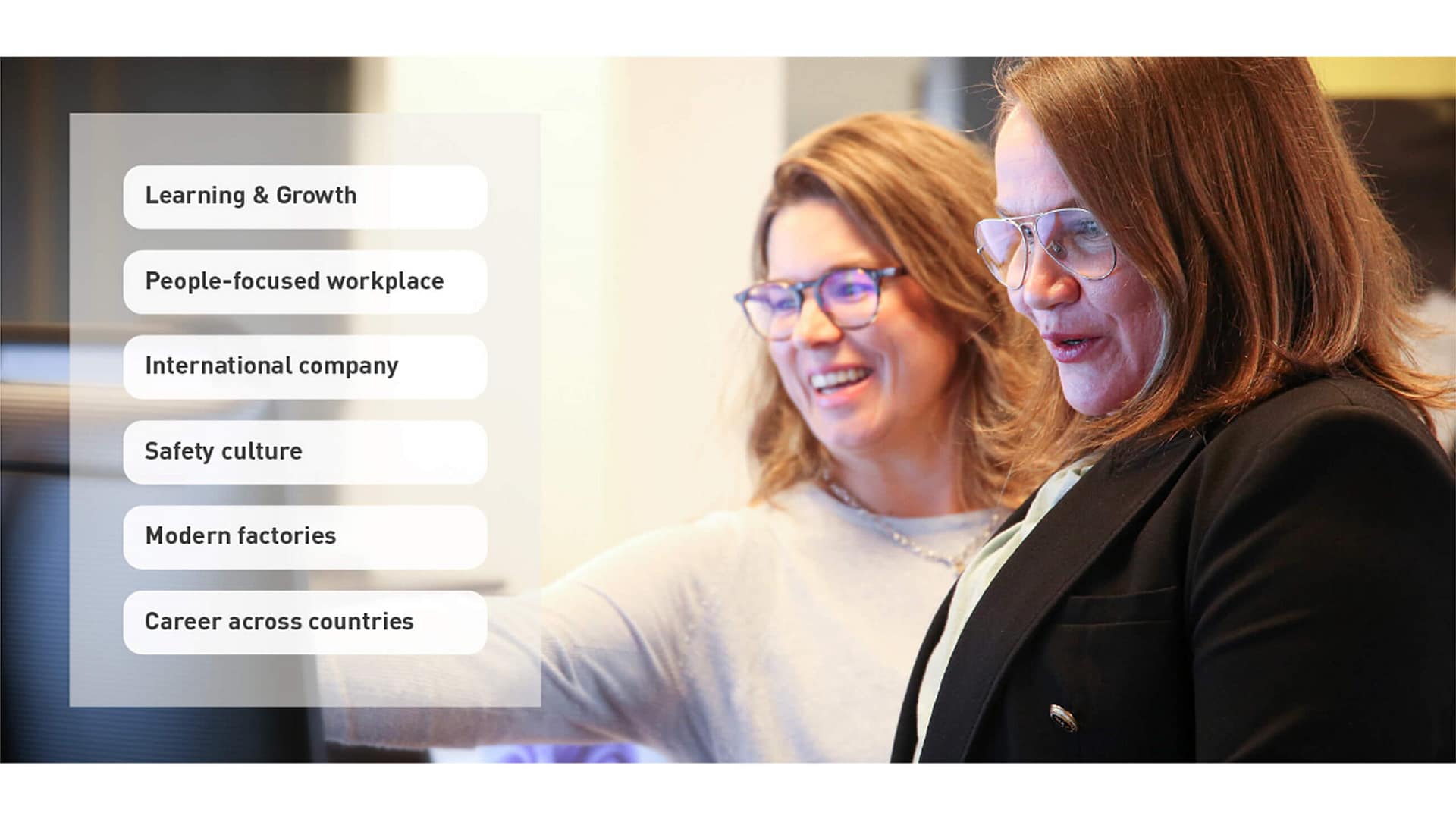 Two women in professional attire smile and interact at a computer screen. On the left, text highlights company values: learning & growth, people-focused workplace, international company, safety culture, modern factories, and career mobility.