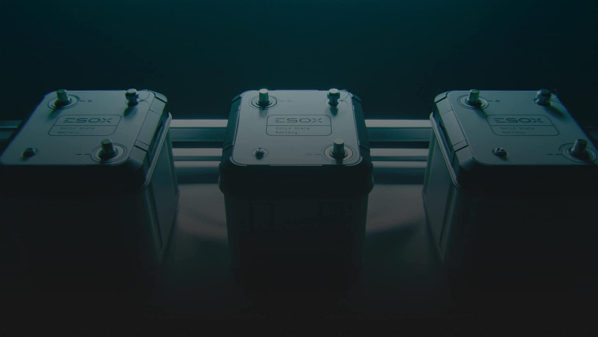 Three industrial battery units labeled "ESOXX SOLID STATE BATTERY" are positioned side by side in a dimly lit environment, with metallic connectors visible on top of each battery.