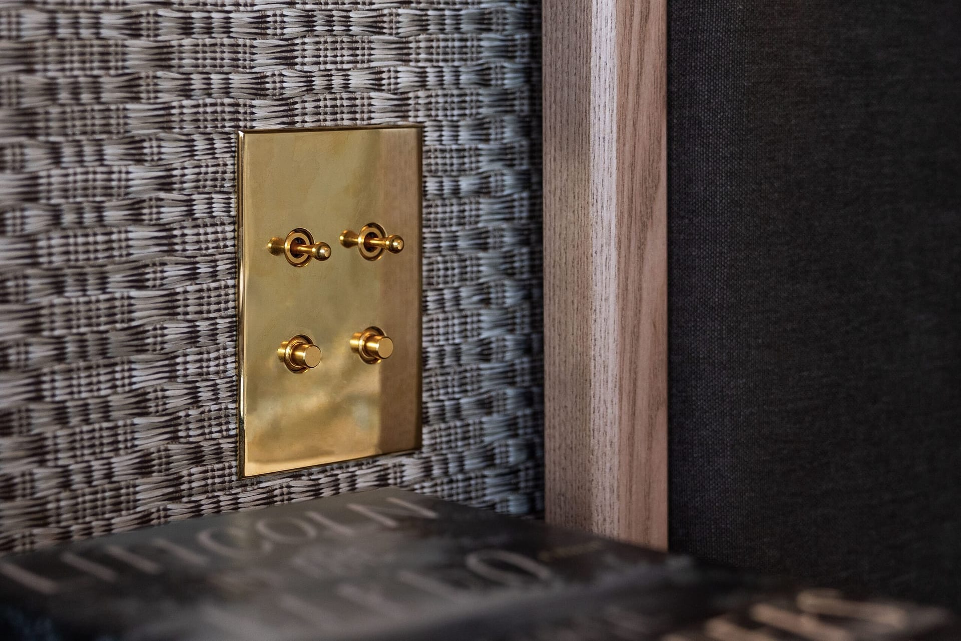 A brass light switch on a wall next to a book.