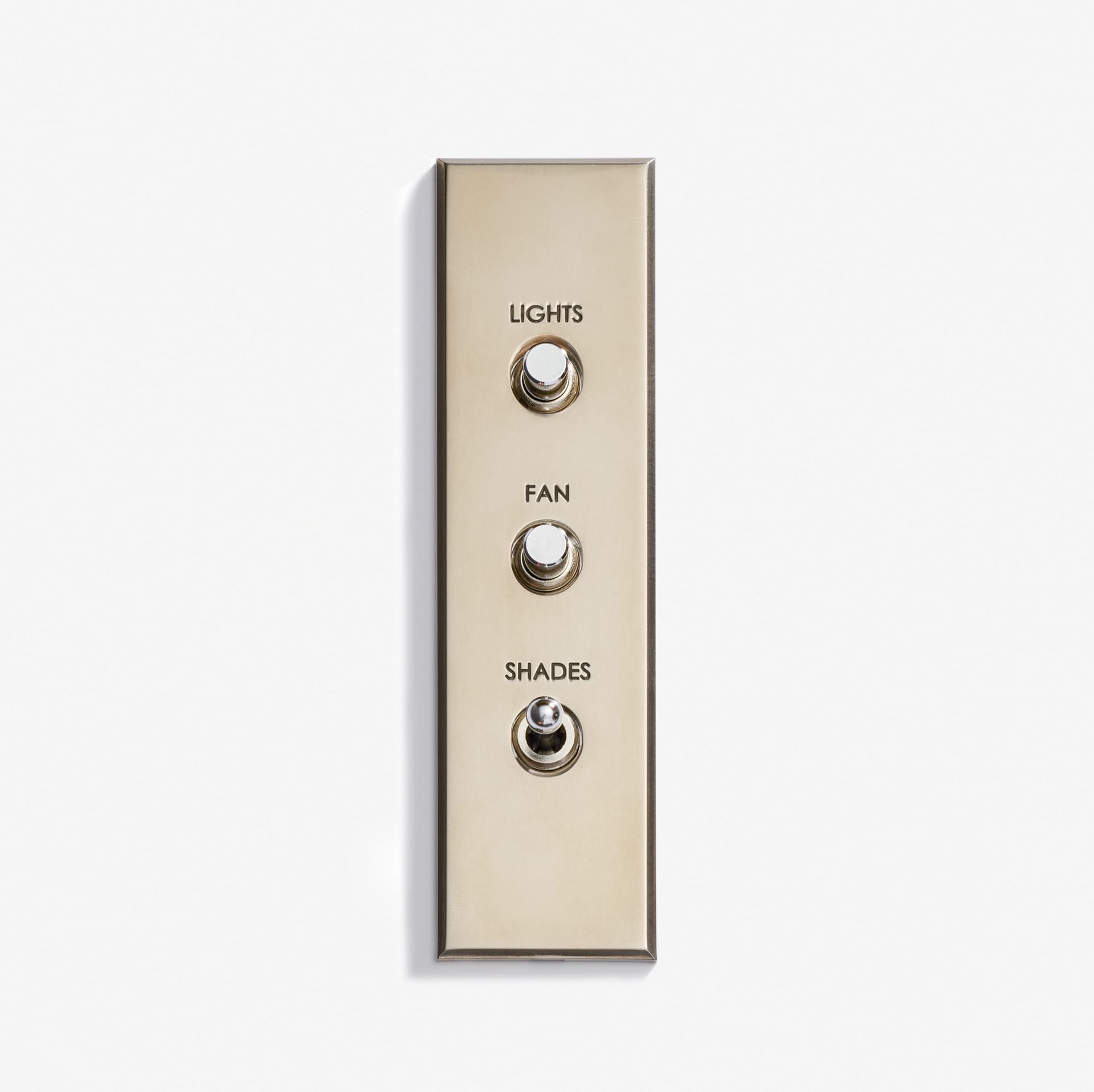 A Luxury Classique Keypad 38 x 133 brass switch panel with three toggle switches labeled "LIGHTS," "FAN," and "SHADES" sits on a white background. All switches are down except the bottom one, which is up.