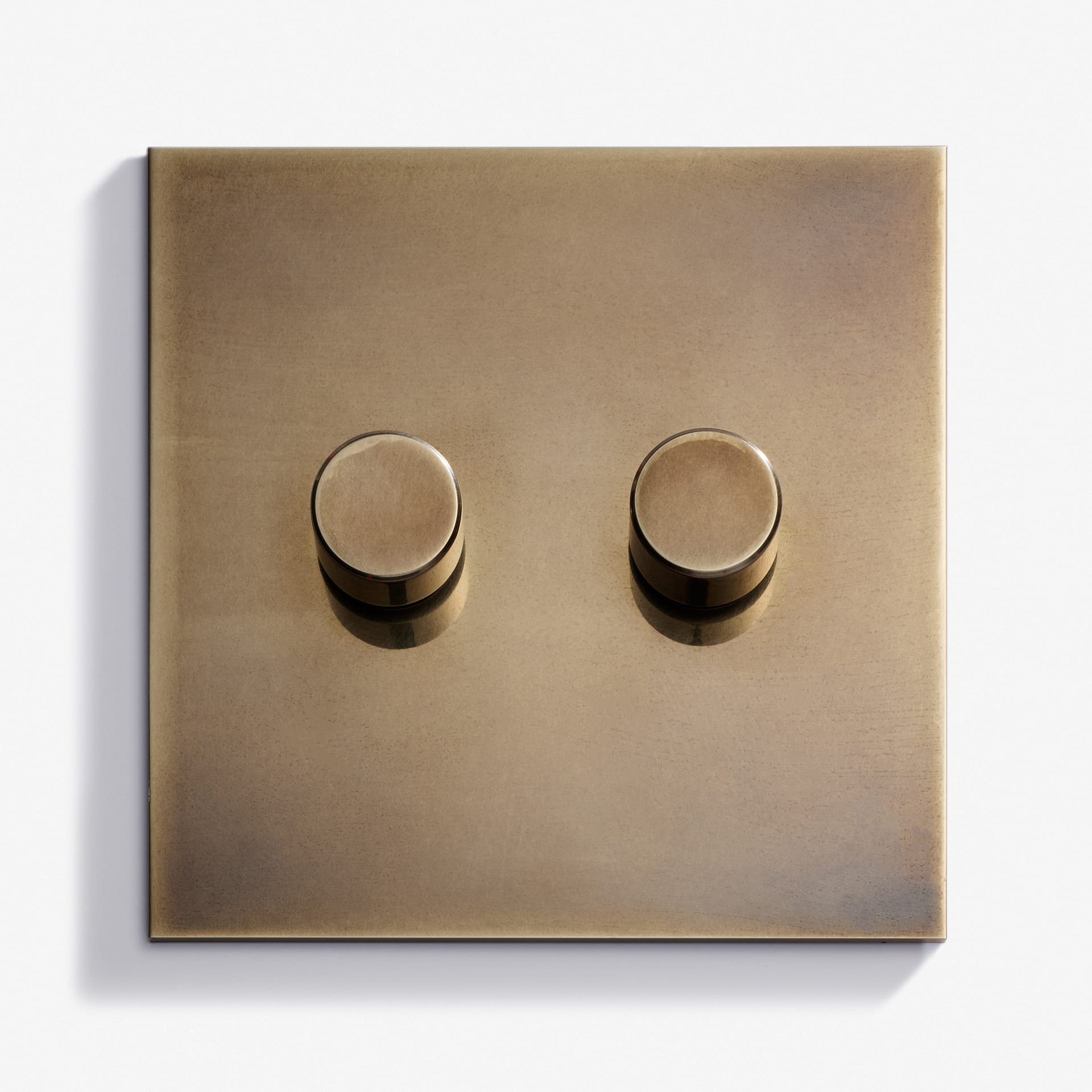A brass double dimmer light switch with two round knobs on a square plate, mounted on a white background.