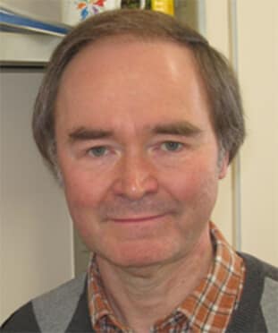 A man in a gray sweater standing in front of shelves.