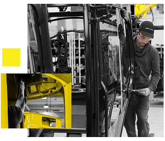 A worker wearing a cap and glasses uses a tool to assemble a large black vehicle part in a factory setting. An inset shows a close-up of another worker’s hand working on a yellow vehicle component.