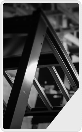 Black and white photo of a metal truss structure shot from a low angle, emphasizing geometric lines and reflections, with a blurred industrial background.