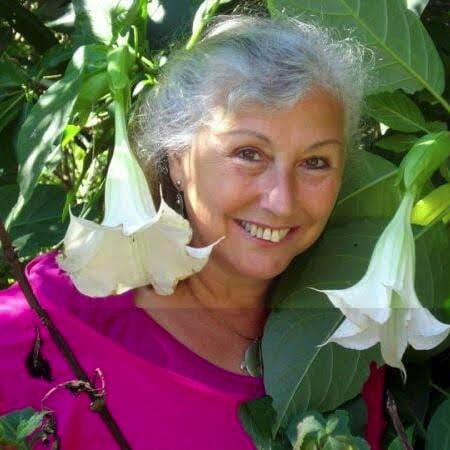 A woman smiling in front of a large plant with white flowers.