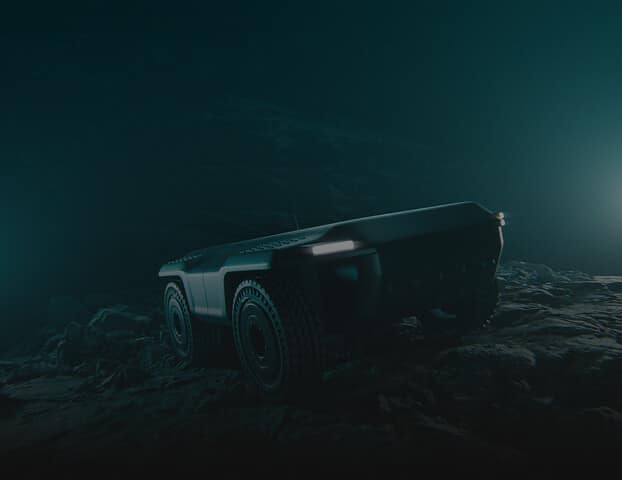 A rugged, autonomous four-wheeled robotic vehicle is illuminated in a dark, foggy environment, driving over rocky terrain with headlights glowing faintly.
