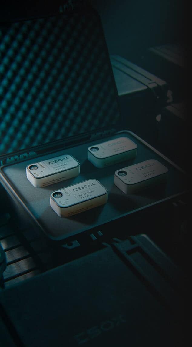 A padded case contains four labeled rectangular devices placed neatly in a foam insert, each labeled “ESOX” and displaying a QR code and additional text on the top surface. The scene has a moody, teal lighting.