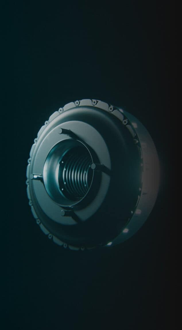 A close-up view of a metallic, circular, turbine-like object with a central spiral structure, illuminated by soft light against a dark background.