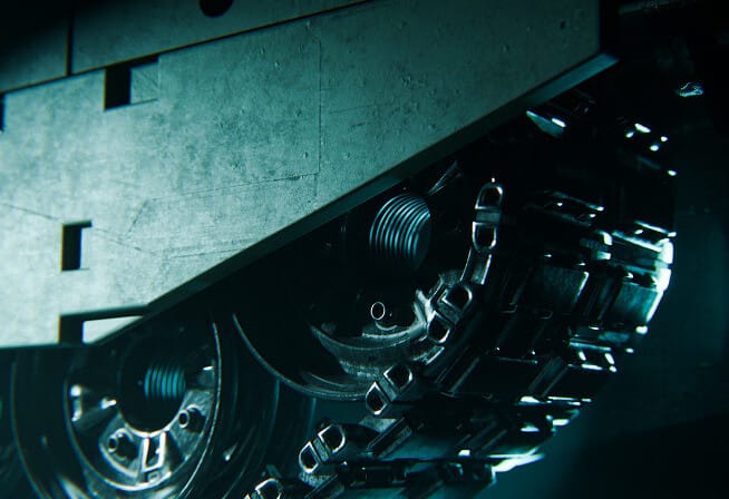 Close-up view of the metal tracks and wheels of a heavy vehicle, likely a tank, shown in dim lighting with a metallic, industrial texture and blue-green highlights.