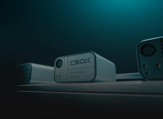 A close-up of a rectangular solid-state battery labeled "ESOX Solid State Battery" with ports visible on its front, placed on a dark surface under teal lighting.