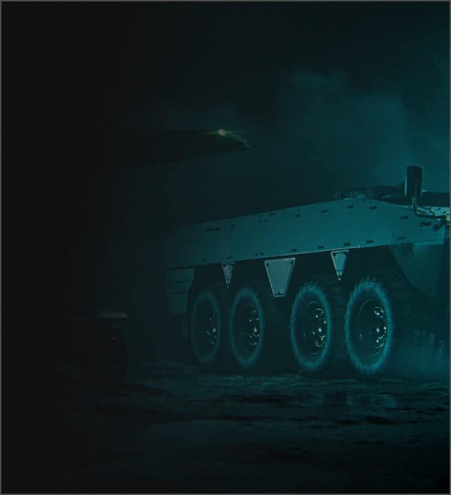 An armored military vehicle with six large wheels is partially visible in dim, smoky lighting, suggesting a nighttime or low-visibility environment. The front of the vehicle is obscured by darkness.