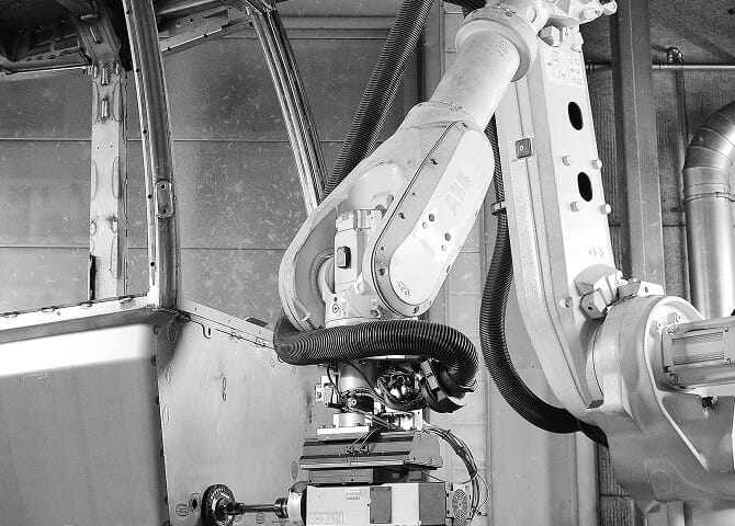 A robotic arm is performing automated work inside a vehicle body in an industrial setting, with various mechanical components and pipes visible in the background.