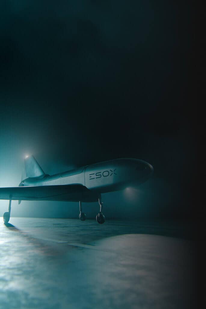 A sleek, modern drone with "ESOX" written on its side stands on a runway in dramatic, low lighting and fog, creating a mysterious, futuristic atmosphere.