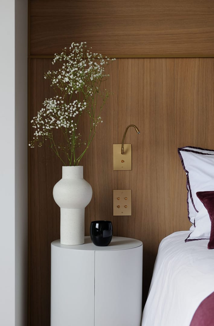 A white bed with a vase of flowers next to it.