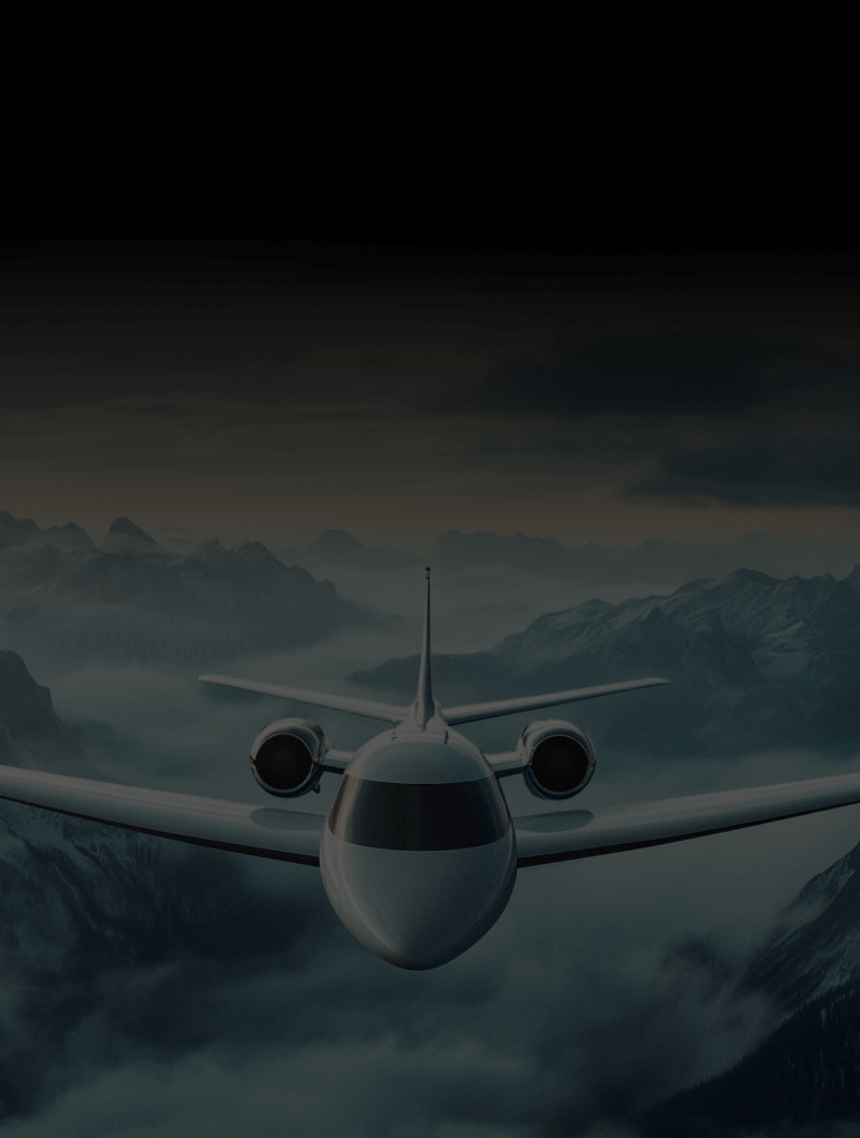 A sleek white airplane flies over scenic mountain ranges partially covered in mist, with a dramatic dark sky above. The aircraft is centered, showcasing its streamlined design against the rugged terrain.