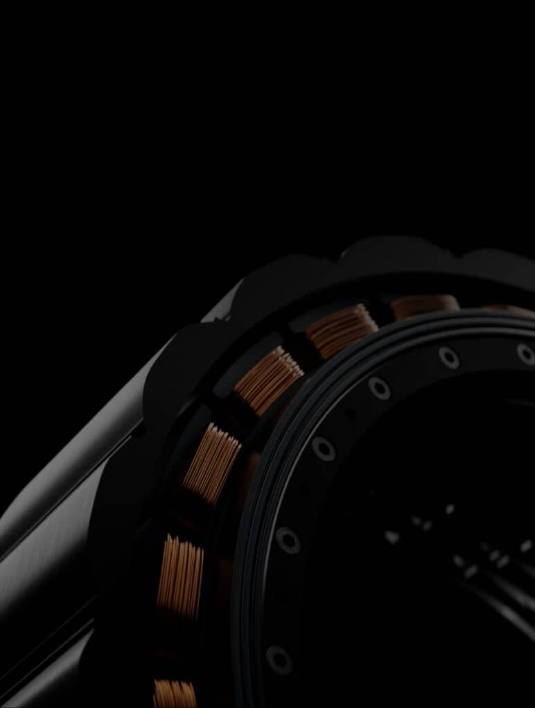 Close-up of a mechanical component featuring copper coils arranged in a circular pattern within a dark, metallic structure. The lighting highlights the texture and intricate details of the coils against a black background.