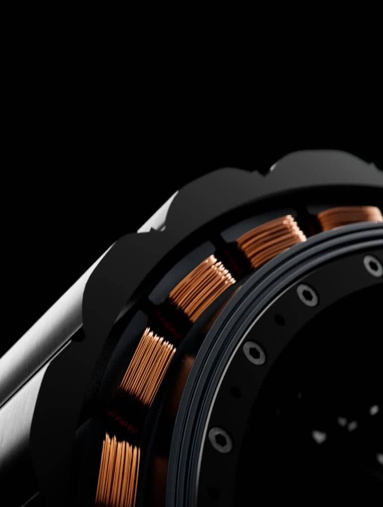 Close-up of a mechanical component showcasing intricate copper coil windings set against a dark background. The image highlights the precision and craftsmanship involved in the engineering of the part.